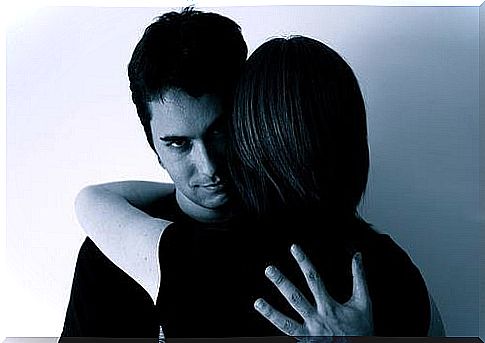 A man looks mockingly at the camera while hugging a woman