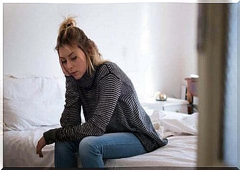 A woman sits tired on the edge of her bed