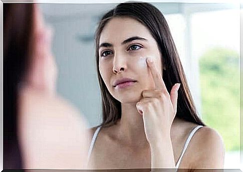 A woman applies cream to her face